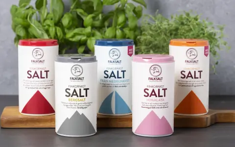 Fem olika tipos de sal från Falksalt: finkornigt, bergsalt, havssalt, Himalaya och jodberikat. Gröna örter i bakgrunden.