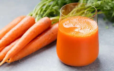 Färskt morotsjuice i ett glas, bredvid en hög med morötter. Morotsjuice är bra för synen och immunförsvaret.