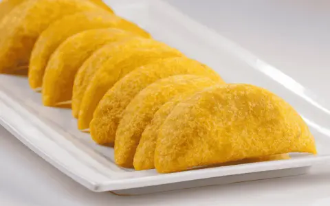 En rad gyllene empanadas de plátano ligger på en vit rektangulär bricka.