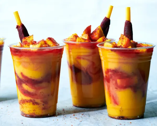 Färgglada mangodrycker med chili och fruktbitar. En perfekt guide för como hacer mangoneadas!