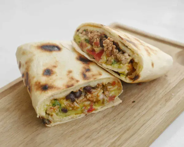 Två halverade burritos de carne med köttfärs, bönor, ris och grönsaker på en träskärbräda.