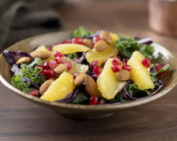 En färgstark sallad med apelsinklyftor, granatäppelkärnor, mandlar och olika typer av lechuga som grönkål och rödkål.