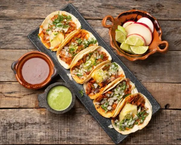 Tacos al pastor med saftig fläskkött, ananas, lök och koriander. Serveras med salsa verde, bönor och lime.