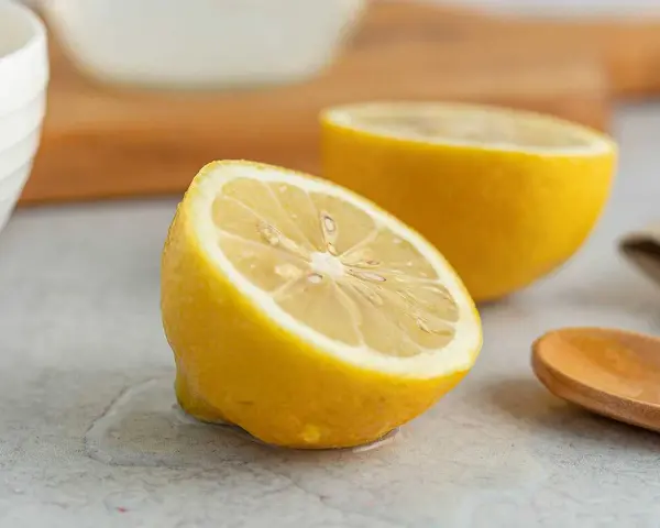 Två halvor av en saftig citron ligger på en grå yta. En träsked ligger bredvid. Perfekt för att pressa ut lite jugo de limón.