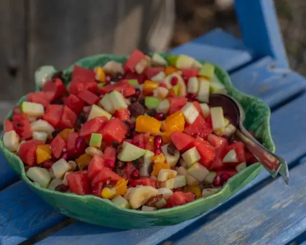 En stor skål med en färgglad ensalada de frutas, fylld med vattenmelon, äpple, apelsin, banan och granatäpple.