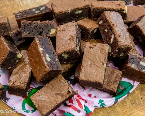 En hög med saftiga, hembakade pasteles de chocolate, vissa med nötter, ligger på ett mönstrat papper.