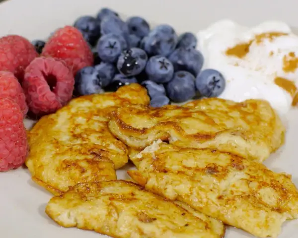 En tallrik med gyllene pannkakor, färska hallon, blåbär och en klick yoghurt med kanel. Perfekt för cenas para diabeticos.