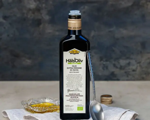 En flaska Zeta Hälsoliv Ekologisk Olio Extra Vergine di Oliva, perfekt aceite de oliva para cocinar. En sked och en liten skål med olja syns också.