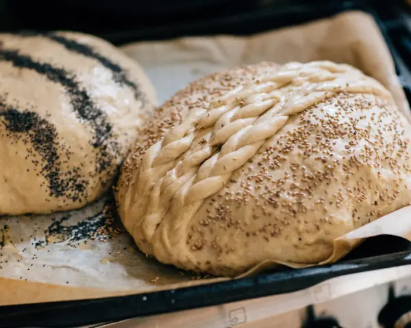 Två olika tipos de pan dulce, en med vallmofrön och en flätad med sesamfrön, redo att bakas.