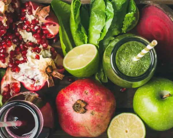 En låda med färska frukter och grönsaker, inklusive granatäpplen, äpplen, lime, rödbetor och gröna smoothies. Perfekt för naturliga botemedel mot gastrit.
