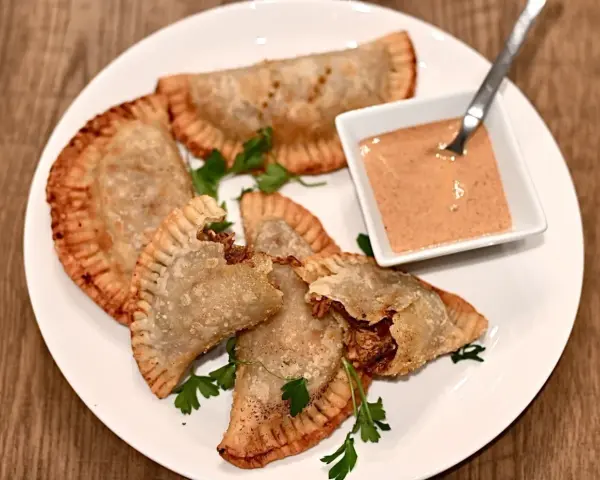 Friterade pastelitos de pollo med en krämig dippsås och persilja på en vit tallrik.
