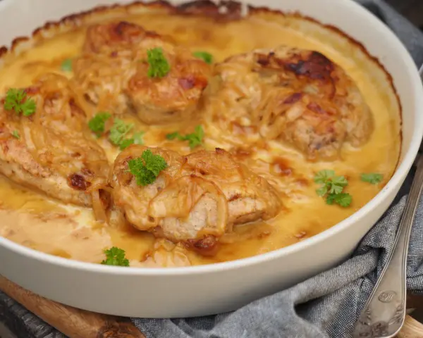 En ugnsform med saftig pollo encebollado salvadoreño, kyckling i en krämig löksås, garnerad med persilja.