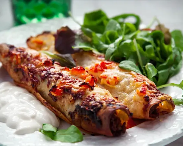 Två gyllene enchiladas, en typisk maträtt från Guatemala, serveras med en fräsch sallad och en klick gräddfil.