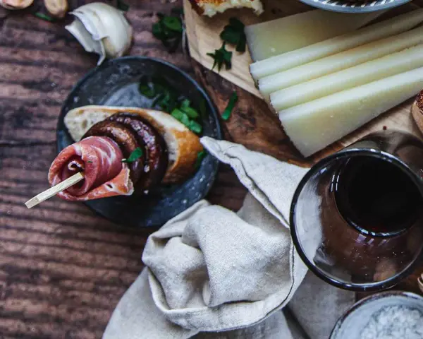 En läcker pinchos de carne med prosciutto, bröd och en skiva korv, serverad med ost och rödvin.