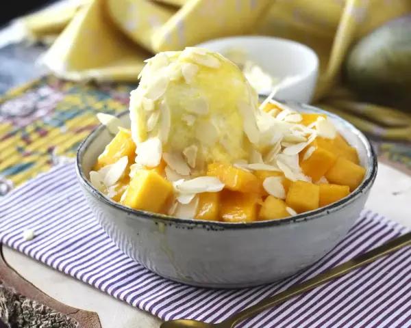 En skål med tärnad mango och en kula vaniljglass, toppad med mandelflagor. En härlig mango en miel-dessert.