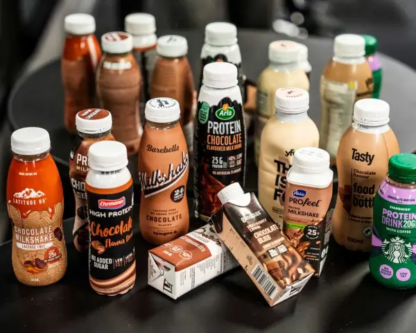 En samling flaskor och kartonger med olika sorters batido de proteinas, mestadels chokladsmak.