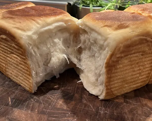 Mjukt och fluffigt **pan de leche** som brutits isär på en träskärbräda. Den gyllene skorpan kontrasterar mot det vita, trådiga inkråmet.