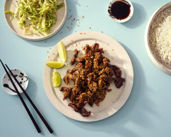 Krispiga chicharrones de cerdo med sesamfrön, serverade med ris, sallad och limeklyftor.