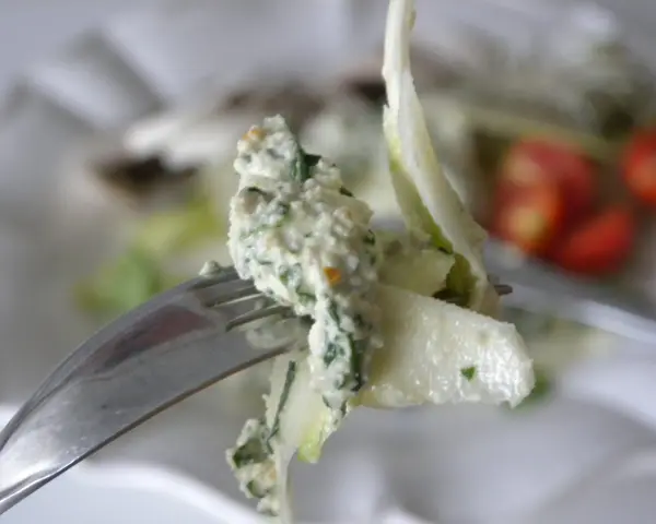 En gaffel med en krämig sallad, kanske med inslag av papayakärnor, nära körsbärstomater.