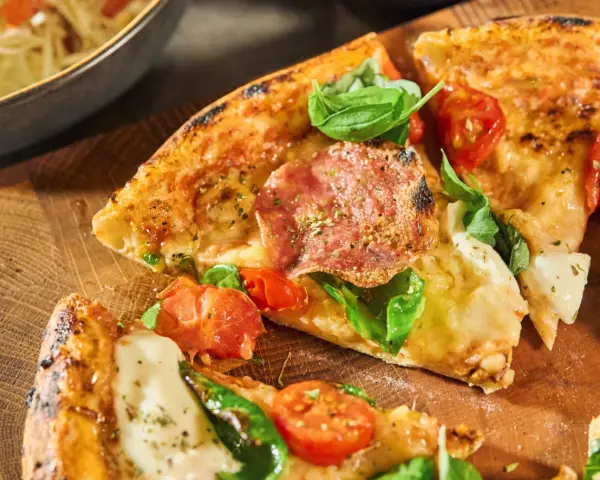 Njut av en utsökt pizza med färska **ingredientes para pizza** som salami, tomater och basilika, serverad på en träskärbräda.