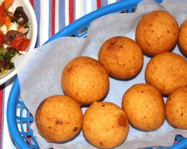Gylla gyllenbruna friterade bollar, som visar hur man gör buñuelos, i en blå korg. Bredvid en skål med en färgglad sallad.