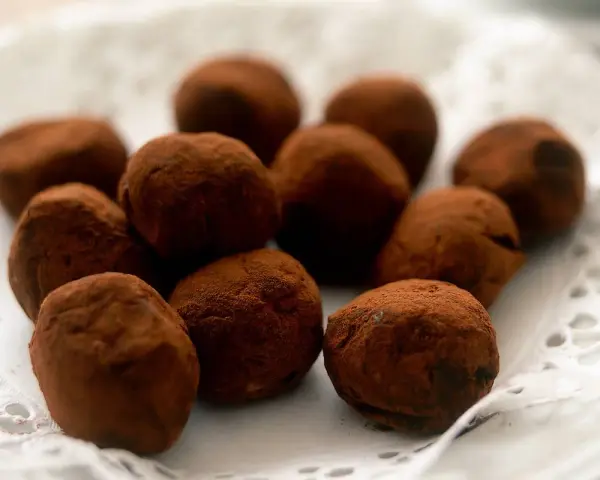 En hög med chokladtryfflar, pudrade med kakao, ligger på en vit spetsduk.