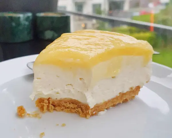 En bit krämig cheesecake med gul topping, perfekt för den som vill lära sig como hacer un cheesecake.