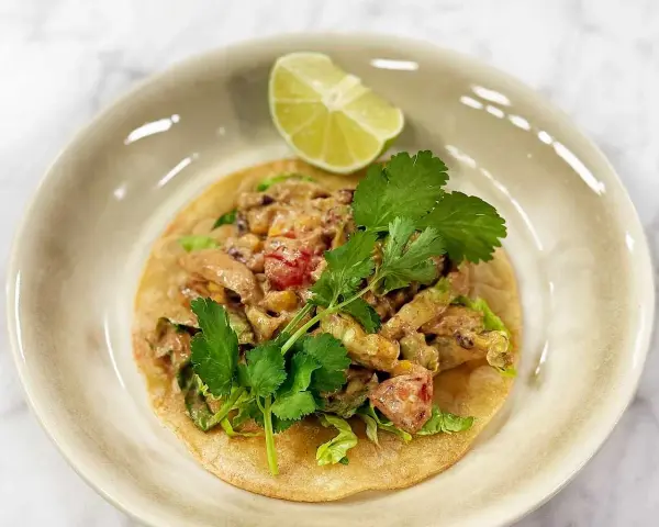 En läcker tostada de pollo med kyckling, majs, tomat och koriander, toppad med en limeklyfta.