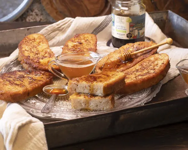 Gylla, gyllene torrejas en miel, serverade på ett fat med honung och en honungsstav.