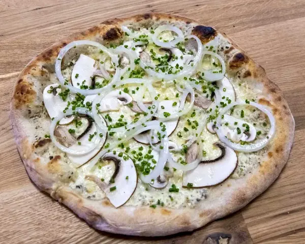 En pizza de hongos med tunna skivor champinjoner, lökringar och gräslök på en träbakgrund.