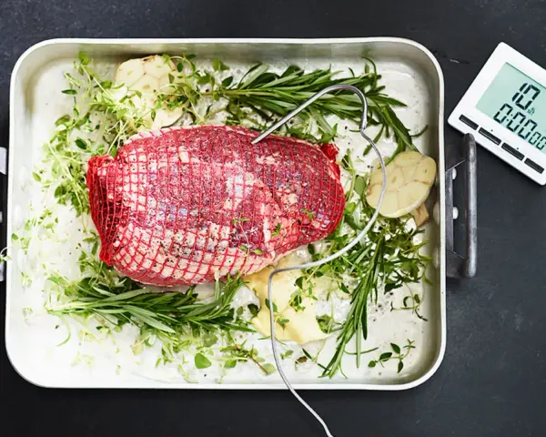 Råstek med örter och vitlök, redo för ugnen. En köttermometer visar 10°C.
