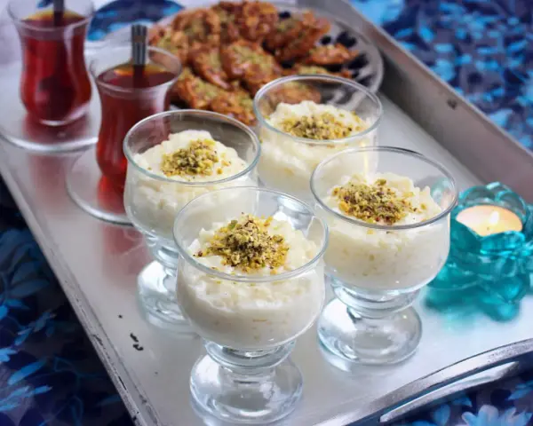 Fyra glas med krämig arroz en leche salvadoreño, toppad med pistagenötter. Två glas med te och en ljuslykta fulländar serveringen.