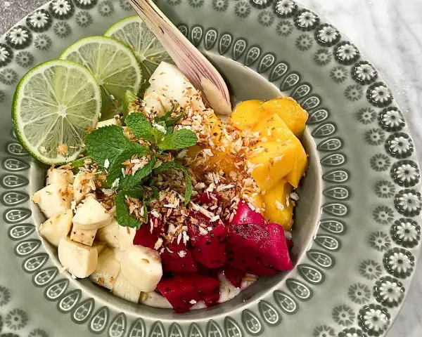 Fruktskål med mango, drakfrukt, banan, lime och mynta, toppad med rostad kokos. En härlig frukost som påminner om dulce de nance.