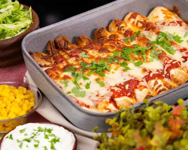 Enchiladas i ugnsform, toppade med smält ost och persilja. Tillbehör: majs, sallad och gräddfil. Perfekt för en middag med tortillas para enchiladas.