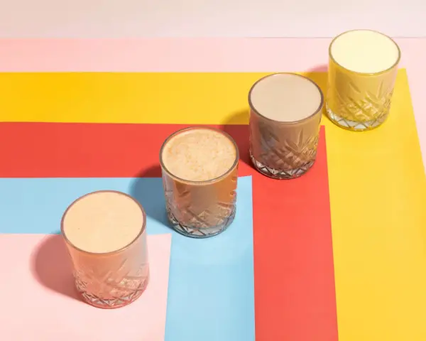 Fyra glas med olika **licuados para bajar de peso** står på en färgglad bakgrund i rött, gult, rosa och ljusblått.