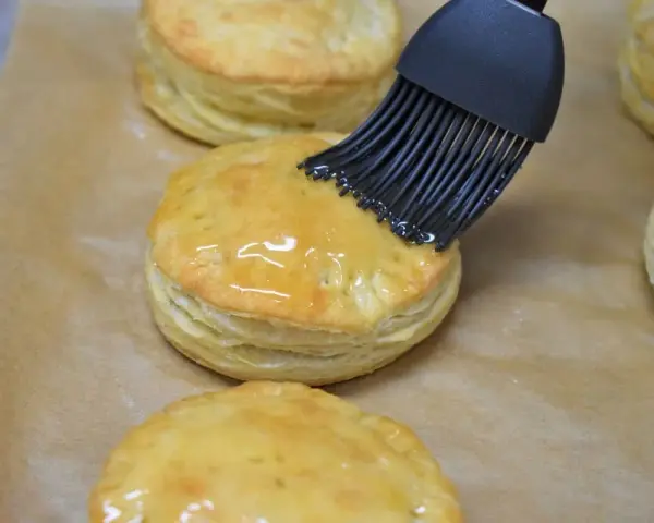 Pensel applicerar glansig glasyr på gyllene, flagnande pastelitos de carne.