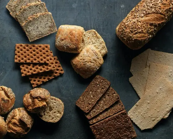 En variation av olika tipos de pan: mörkt rågbröd, knäckebröd, surdegsbröd och frallor.