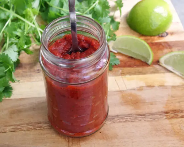 En burk med hemlagad salsa para tacos, med färsk koriander och limeklyftor på en träskärbräda.