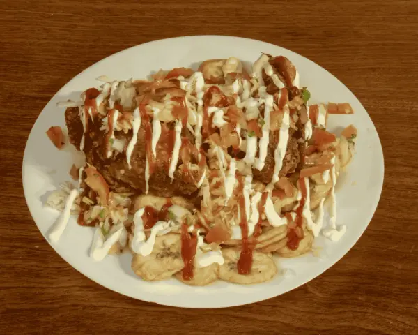 En tallrik med pollo chuco: friterad kyckling, stekta bananer, kål, tomat och majonnäs.