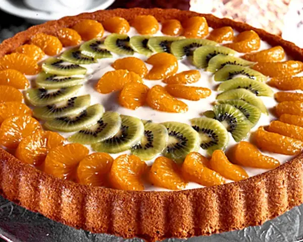 En vacker tartaleta de frutas med mandarinklyftor och kiwiskivor arrangerade i ett mönster på en krämig fyllning.