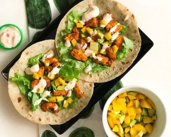 Två kycklingwraps med mango, avokado och sallad. En liten skål med mangosalsa. Hur många kalorier har en tortilla?
