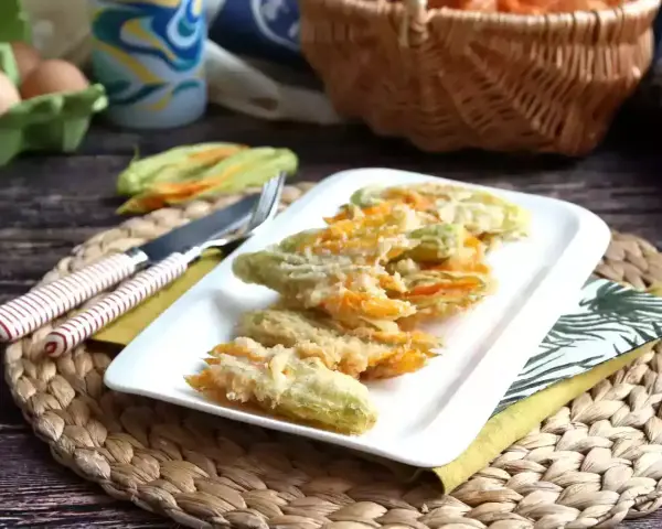 Friterade flor de calabaza på en vit tallrik, redo att avnjutas. Bredvid ligger en kniv och gaffel.