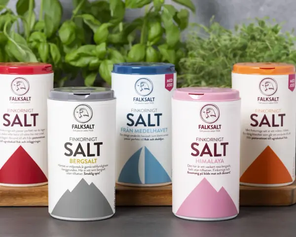 Fem olika tipos de sal från Falksalt: finkornigt, bergsalt, havssalt, Himalaya och jodberikat. Gröna örter i bakgrunden.