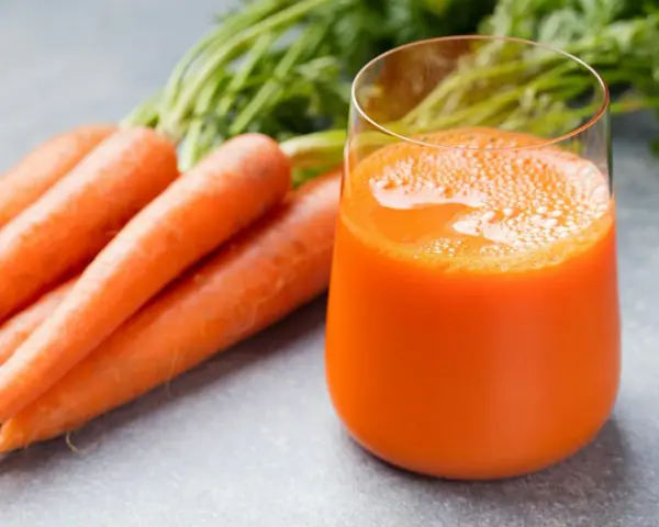 Färskt morotsjuice i ett glas, bredvid en hög med morötter. Morotsjuice är bra för synen och immunförsvaret.