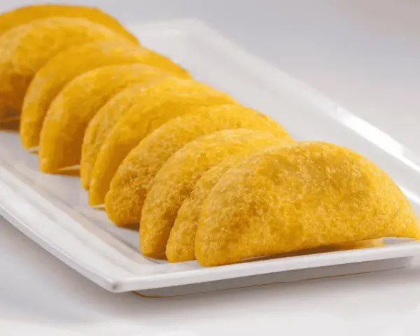 En rad gyllene empanadas de plátano ligger på en vit rektangulär bricka.