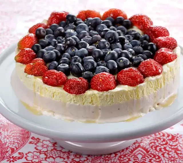 En vacker pastel de cumpleaños, toppad med färska jordgubbar och blåbär, ser utsökt ut på ett vitt tårtfat.