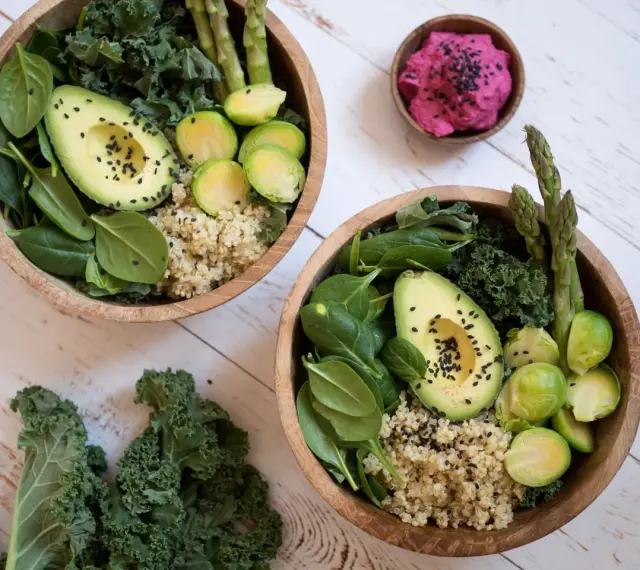 Två skålar med quinoa, spenat, grönkål, avokado, brysselkål och sparris. En liten skål med rosa röra. Perfekt för en **comida saludable**.