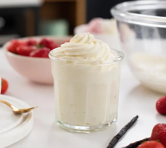 En krämig crema chantilly i ett glas, omgiven av färska jordgubbar och vaniljstänger. Perfekt för sommardesserter.