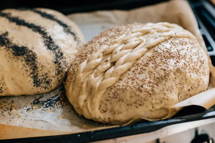 Två olika tipos de pan dulce, en med vallmofrön och en flätad med sesamfrön, redo att bakas.
