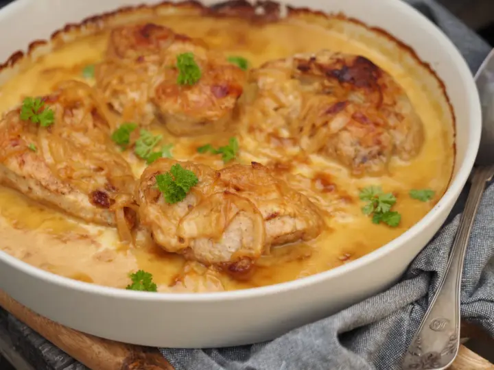 En ugnsform med saftig pollo encebollado salvadoreño, kyckling i en krämig löksås, garnerad med persilja.